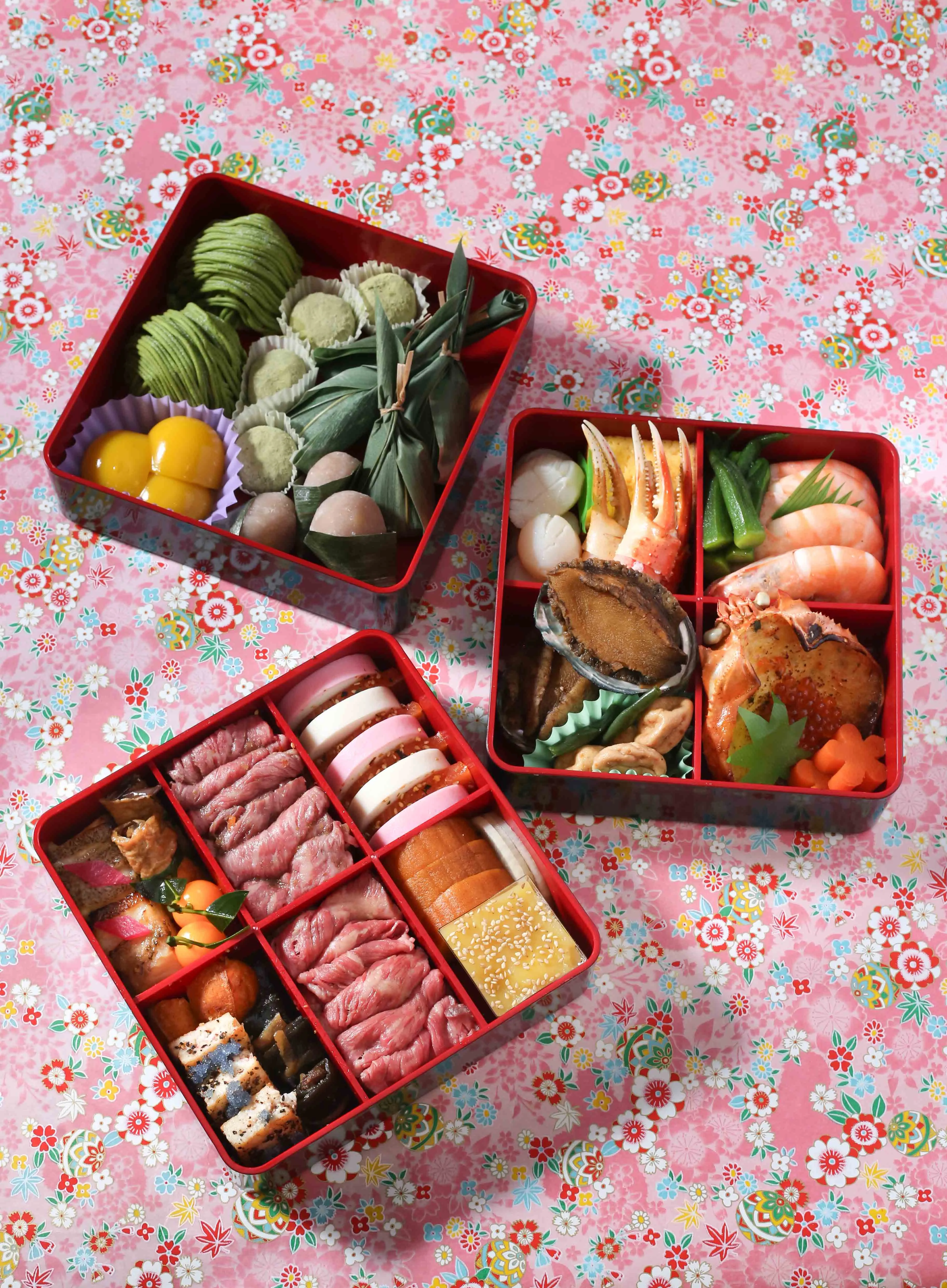 Overhead view of three red Osechi boxes filled with Japanese New Year foods.