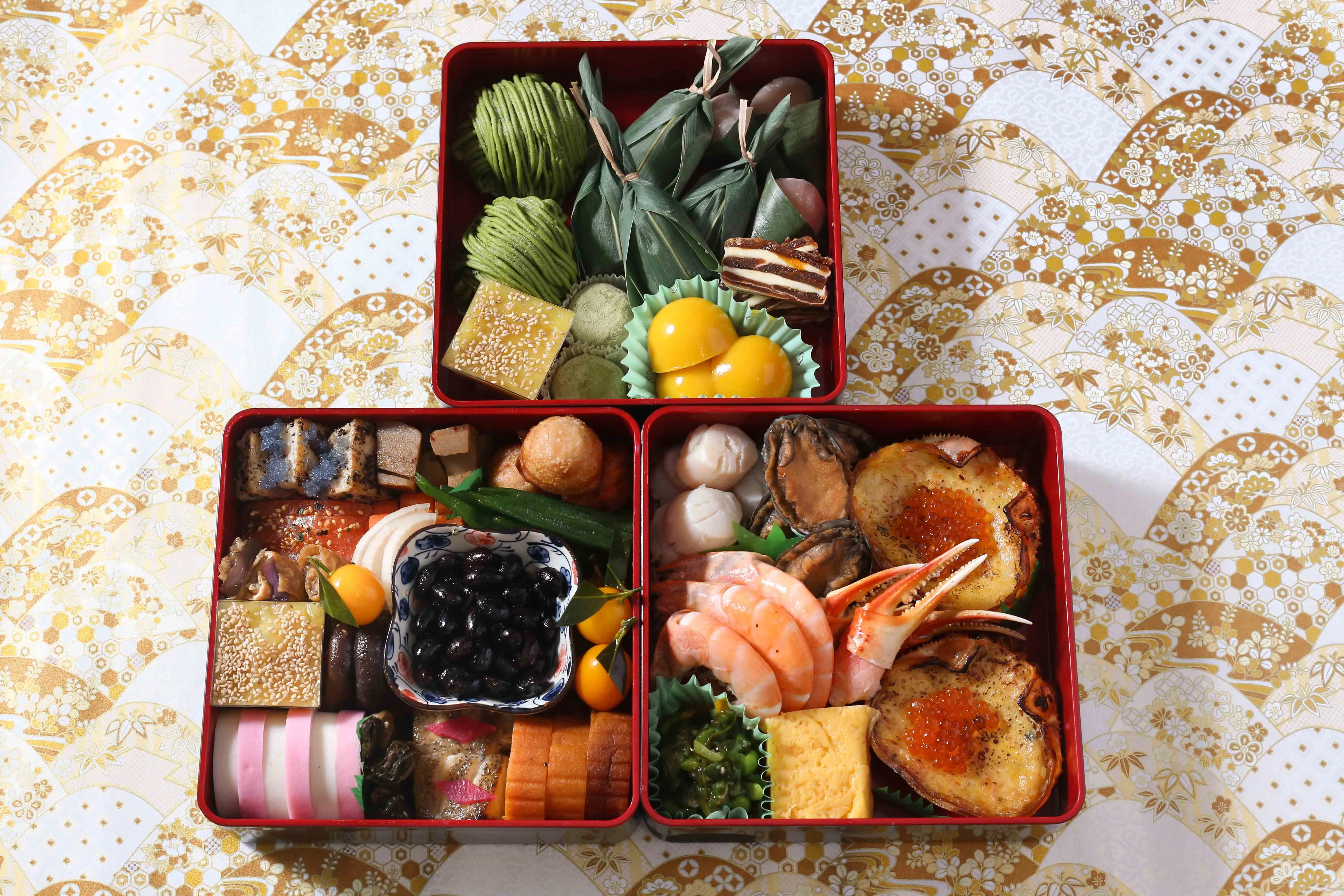 A traditional Japanese Osechi Ryori feast in red lacquer boxes, featuring various savory and sweet dishes.