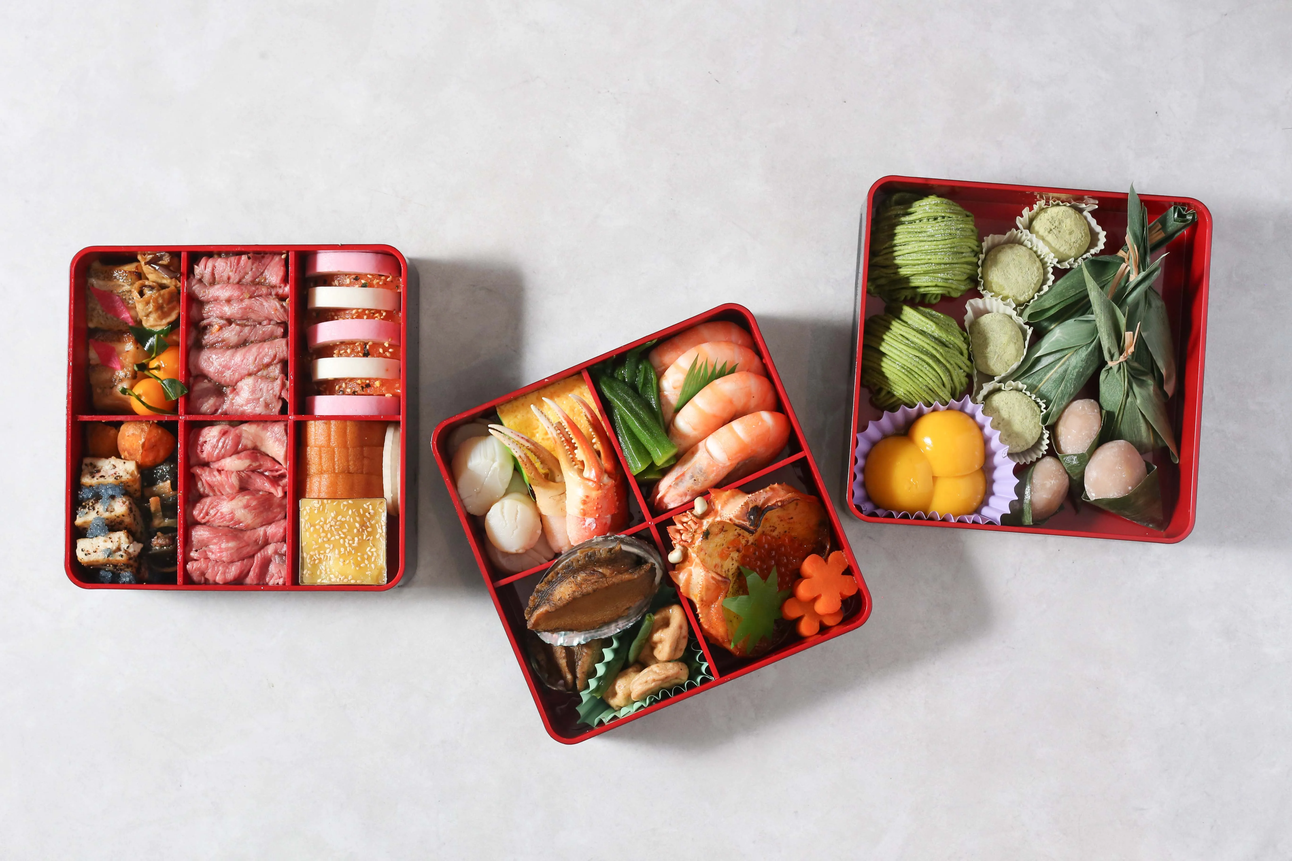 Overhead view of three red osechi boxes filled with Japanese New Year's delicacies.