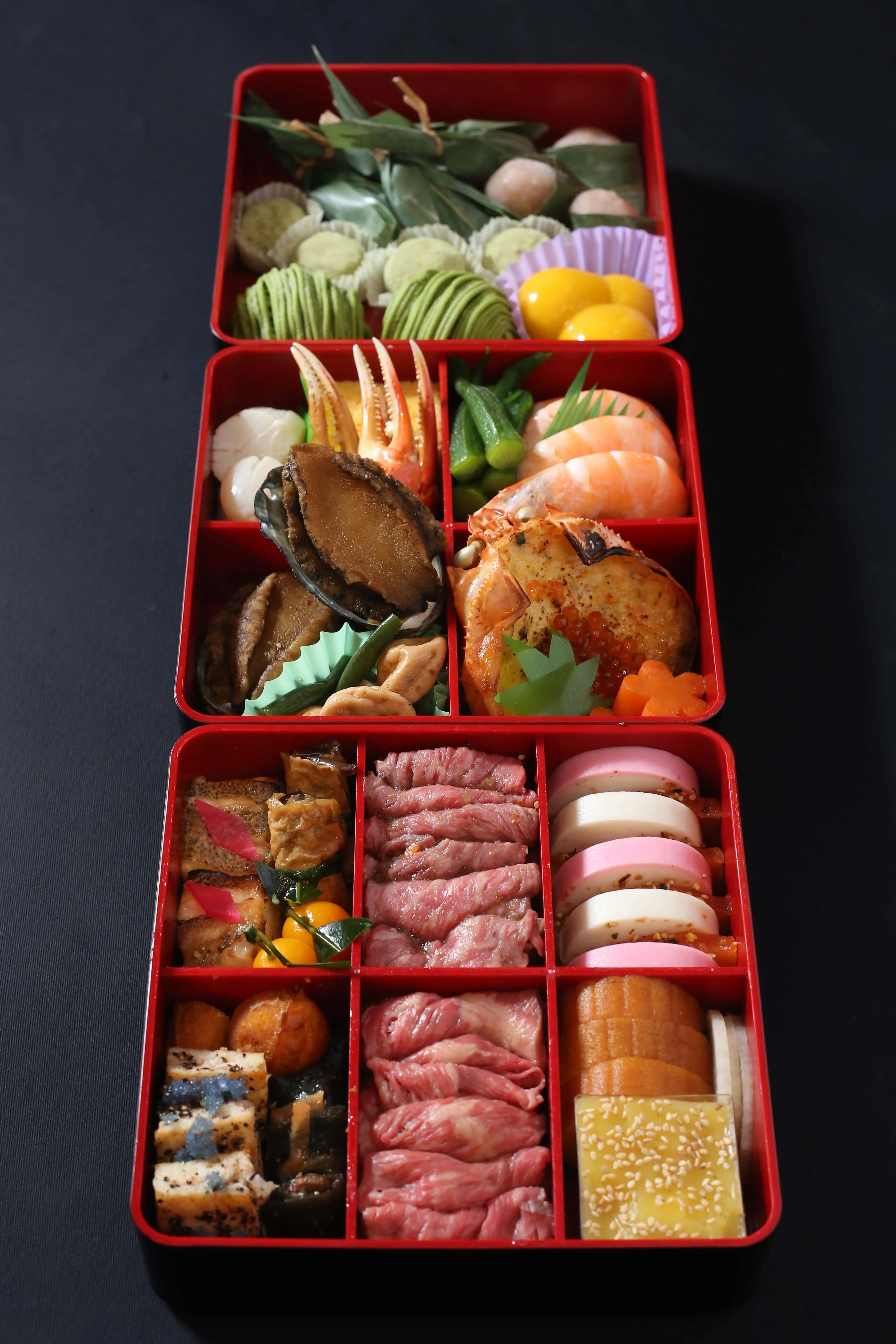 A stacked red osechi box filled with a variety of traditional Japanese New Year foods.