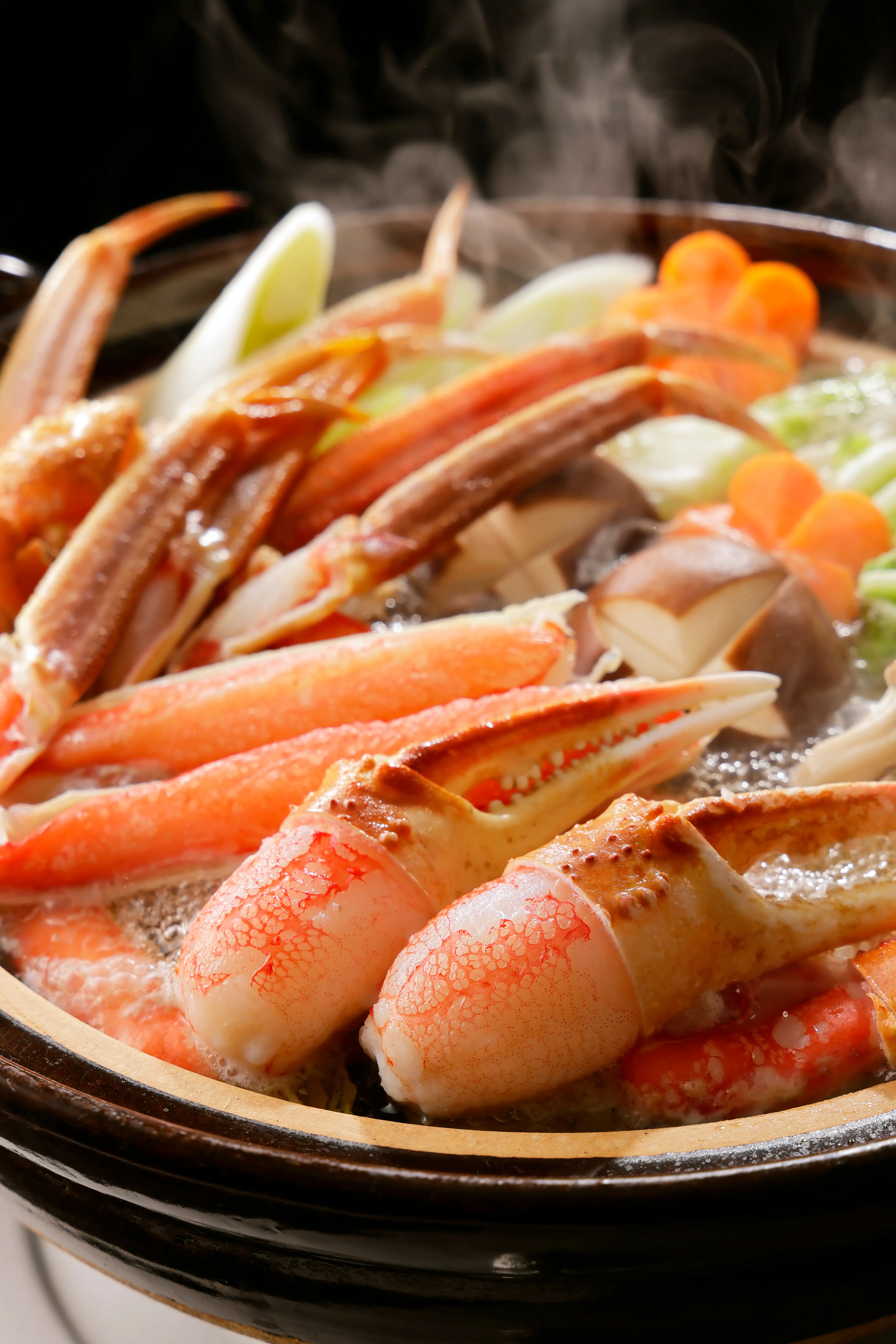 A close-up shot of a steaming hotpot filled with vibrant orange snow crab legs, claws, green vegetables, and mushrooms in a rich broth.